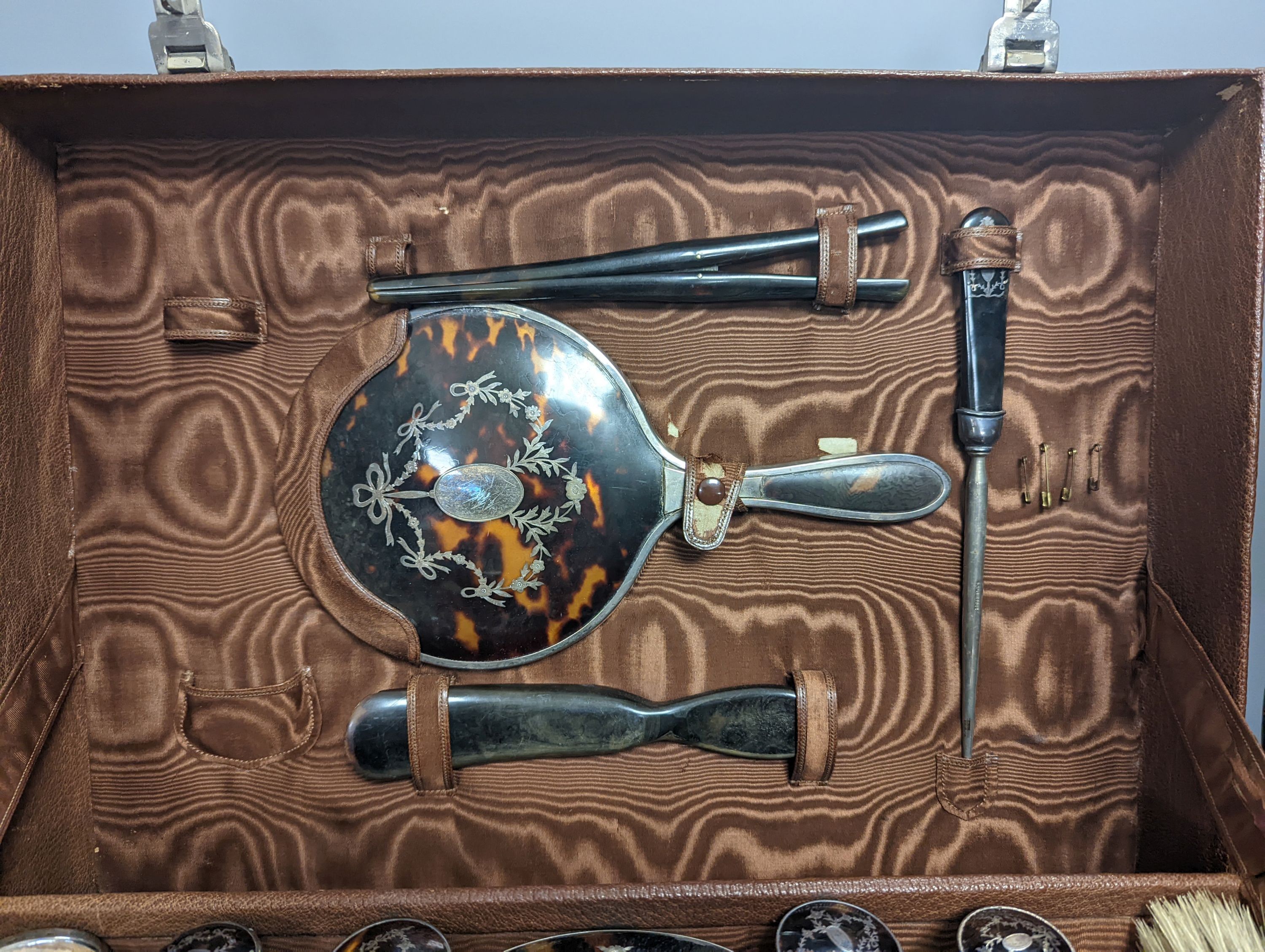 A George V leather travelling toilet case, containing twenty one matched, mainly silver and tortoiseshell pique items including toilet jars, brushes, mirror and pocket watch holder, mostly Levi & Salaman, Birmingham, 191